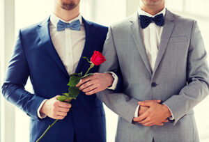 people, homosexuality, same-sex marriage and love concept - close up of happy male gay couple with red rose flower holding hands on wedding